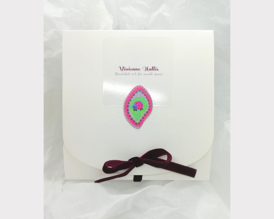 Small square shaped white gift box with purple velvet ribbon with a painted ladybird motif that your artwork will arrive in