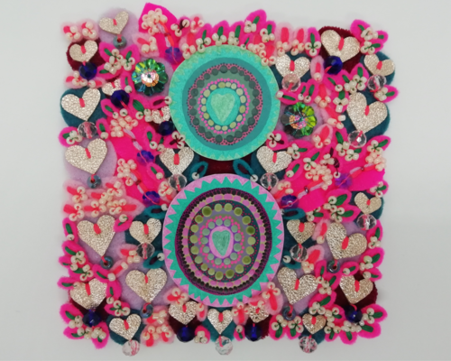 A romantic textile art featuring two painted concentric circles which each contain a heart motif and are surrounded by gold fabric hearts and stitched beads